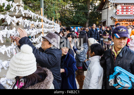 Giappone, Nishinomiya santuario, Capodanno, Shogatsu. Persone nella parte anteriore del telaio funziona con molti abbandonato Omikuji papers on, la legatura proprio a. Foto Stock