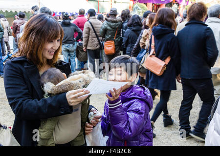 Nuovo anno a Nishinomiya santuario, Giappone. Giovane madre con bambino in vettore contro il suo torace, sorridente come lei e suo figlio a leggere un omikuji fortune di carta. Foto Stock