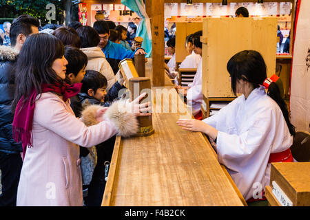 Giappone, Nishinomiya santuario, anno nuovo giorno, Shogatsu. Donna acquisto omikuji fortune paper da Miko, santuario maiden, al santuario di occupato ufficio, Shamusho. Foto Stock