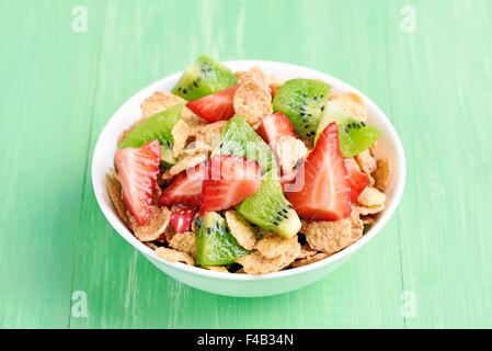 Fiocchi di mais con fragole fresche e kiwi fette nella ciotola sul tavolo verde Foto Stock