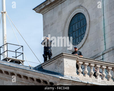 I funzionari di polizia con un binocolo guardano fuori dal tetto di St Martin-in-the-Fields Church come ufficiali con cani poliziotto di pattuglia sulla strada sottostante prima del settantesimo vittoria sul Giappone giorno commemorazioni detenute nel centro di Londra. Dotato di: visualizzare, atmosfera Foto Stock