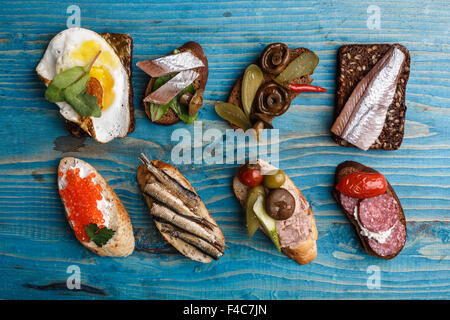 Varietà di aprire panini da cereali integrali e baguette di pane di segale con diversi condimenti oltre invecchiato in legno di colore blu sullo sfondo. Foto Stock
