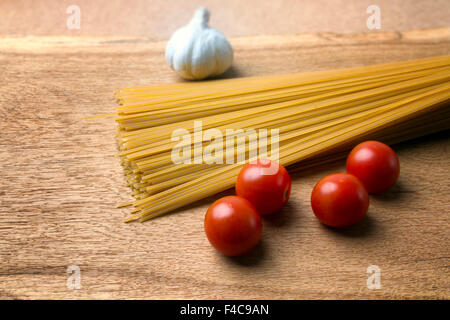 Aglio, i pomodorini cotte e di spaghetti su una tavola di legno Foto Stock