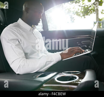 Colpo di giovane imprenditore africani lavorano su laptop all'interno di un'auto. Un socio in affari in viaggio per lavoro in un'auto. Foto Stock