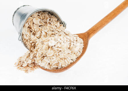 Benna di fiocchi d'avena si sbriciola in un cucchiaio di legno, su sfondo bianco Foto Stock