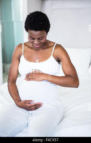 Sorridente donna incinta seduta sul suo letto Foto Stock