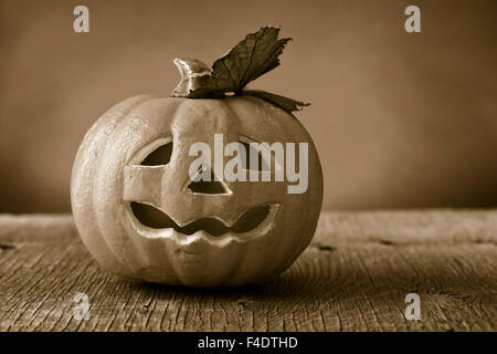Un pauroso zucca scolpito su un rustico di una superficie di legno, in seppia tonificante, con un effetto drammatico Foto Stock
