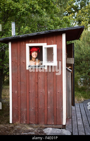 Una donna che guarda attraverso la finestra in una dipendenza, Svezia. Foto Stock