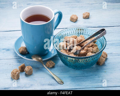 Tazza di tè e zucchero di canna i cubi su vecchio blu tavolo in legno. Foto Stock