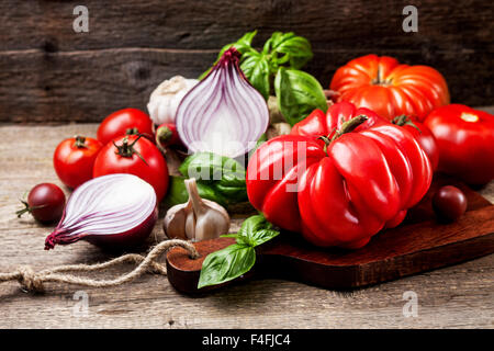 Pomodori freschi, basilico, rosso cipolla, aglio e pepe nero sul vecchio sfondo di legno Foto Stock