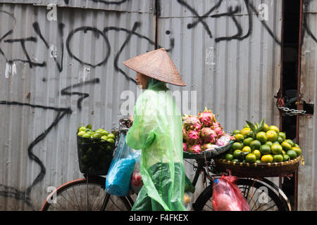 Signora vietnamita per la vendita di frutta da lei in bicicletta in Hanoi old quarter, indossando il mac in plastica per tenere a secco da tempeste,Vietnam Foto Stock