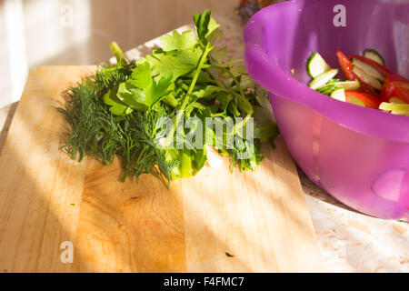 Il prezzemolo e l'aneto sul tagliere di legno. Preparazione di insalata di verdure e ortaggi freschi/insalata fresca con olio d'oliva Foto Stock