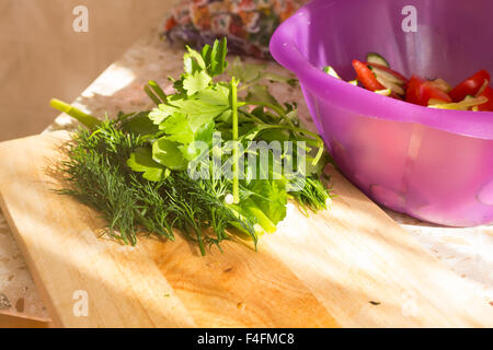 Il prezzemolo e l'aneto sul tagliere di legno. Preparazione di insalata di verdure e ortaggi freschi/insalata fresca con olio d'oliva Foto Stock