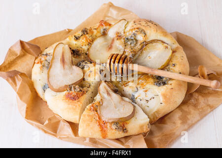 Fette di Pizza con pera, gorgonzola e miele con legno d'ulivo miele bilanciere su carta da forno su bianco tavolo in legno. Foto Stock