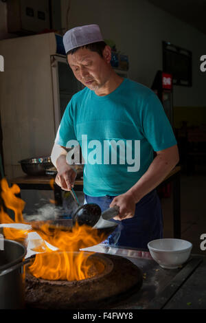 Cuoco cinese nel quartiere musulmano di Xi'an agitazione un wok a una fiammante stufa. Foto Stock