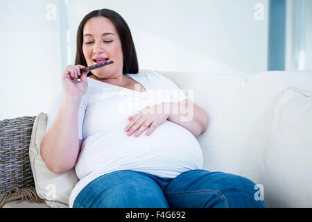 Sorridente donna incinta mangiare il cioccolato Foto Stock