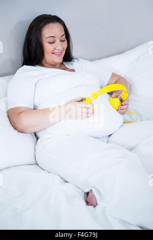 Donna incinta mettendo le cuffie sul suo ventre mentre giaceva su un letto Foto Stock