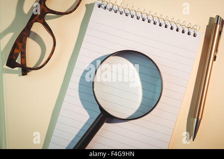 Lente di ingrandimento su notepad tra penna e occhiali Foto Stock