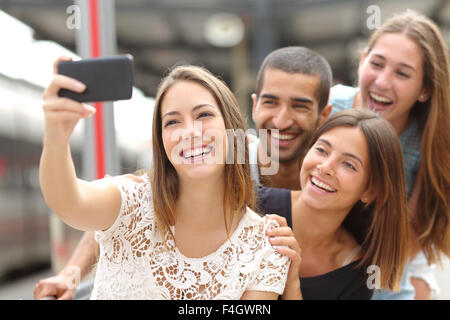 Il gruppo di quattro simpatici amici prendendo selfie con uno smart phone in una stazione ferroviaria in estate Foto Stock