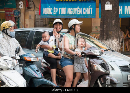 Due madri e due bambini sullo stesso scooter moto attraverso Hanoi city centre, la città capitale del Vietnam. Foto Stock