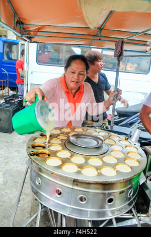 Una donna street food venditore versa la pastella in coppette individuali sul suo biscotto macchina di cottura. Foto Stock