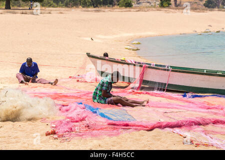 I pescatori locali riassettavano le reti da pesca in riva al lago spiaggia, Kaya Mawa, Likoma Island, il Lago Malawi Malawi, sud-est Africa Foto Stock