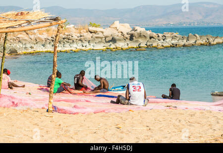I pescatori locali colorati riassettavano le reti da pesca sulla spiaggia in riva al lago, Likoma Island, il Lago Malawi Malawi, sud-est Africa Foto Stock