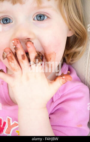 4 anno vecchia ragazza con il cioccolato sulle sue mani e viso Foto Stock