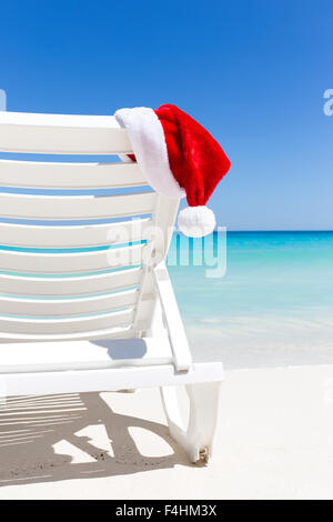 Santa Claus Hat sul lettino vicino alla spiaggia di sabbia con il turchese del mare dei caraibi acqua. Tropical Scheda di Natale Foto Stock