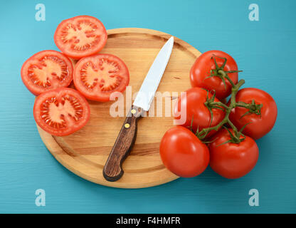 Pomodori maturi, intero e affettato con coltello seghettato sul tagliere di legno Foto Stock