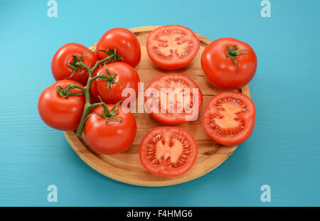 Pomodori freschi - sulla vite, dimezzata e tutto su una circolare tagliere di legno Foto Stock