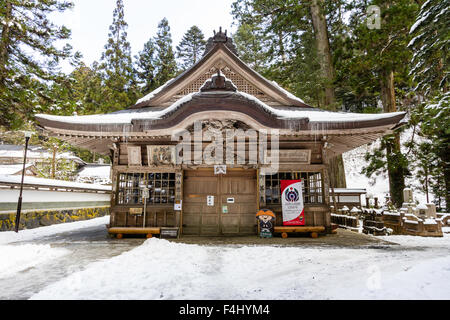 Koyasan, Giappone, Okunoin cimitero, Giappone il più grande. In legno coperto di neve santuario hall con alberi di cedro in background. Ghiaccioli pendenti dal tetto. Foto Stock