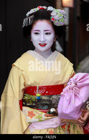 Sorridendo, maiko apprendista geisha, con accappatoi di giallo, si ferma in strada a modo di sera appuntamento, Gion, Kyoto, Giappone, Asia Foto Stock