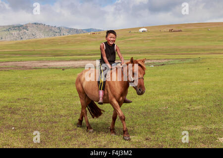 Cavallo e sorridente boy riding bareback con ger e colline dietro ad estate campo nomadi, Khujirt, Uvurkhangai, Mongolia centrale Foto Stock