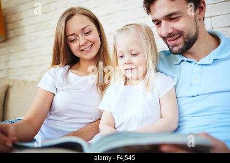 Felice coppia giovane e la loro figlia la lettura a casa Foto Stock