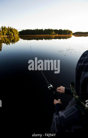 Ragazzo di pesca in un lago calmo al tramonto, Finlandia. Foto Stock