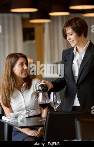 Cameriera di servire un vino alla donna a tavola, sorridente Foto Stock
