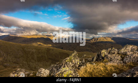 Guardando verso il Langdales con The Langdale Pikes sotto i raggi del sole, dalle pendici del Wetherlam Foto Stock