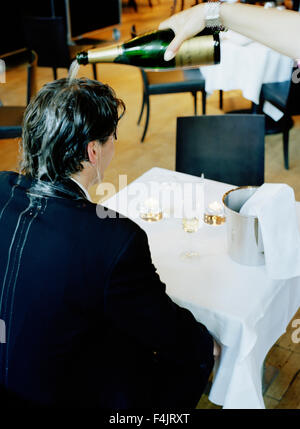 Persona versando champagne sulla testa di uomo in ristorante Foto Stock