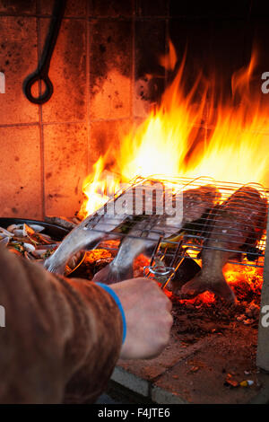 L'uomo cucinare il pesce in un fuoco aperto Foto Stock