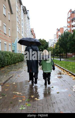La madre e il figlio a piedi attraverso il marciapiede durante la pioggia Foto Stock