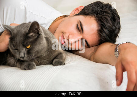 Bel giovane uomo Animal-Lover su un letto, avvolgente e coccole il suo grigio gatto domestico Pet. Foto Stock