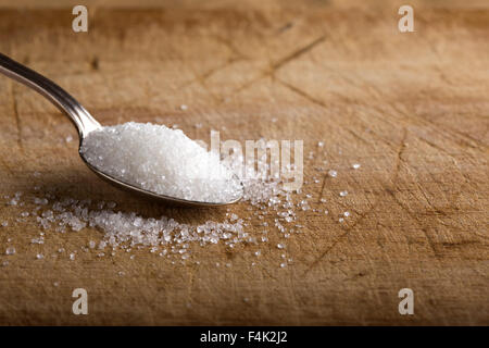 Close-up di zucchero granulato in cucchiaio d'argento su sfondo di legno Foto Stock