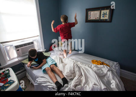 Un giovane ragazzo guarda al suo tablet mentre il suo fratello più giovane fastidiosamente danze sul suo letto Foto Stock