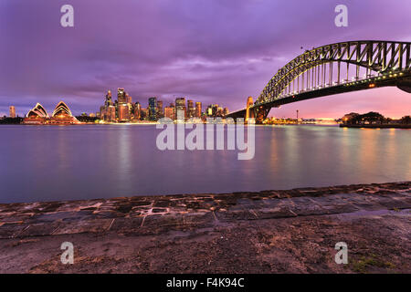 La città di Sydney CBD monumenti illuminati al tramonto e visualizzati attraverso il porto da Milsons Point. Il Sydney Harbour Bridge, grattacieli Foto Stock