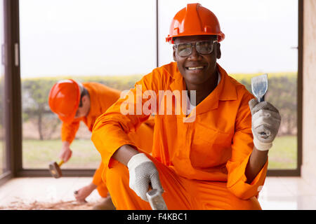 African workman tenendo uno scalpello e un martello dentro casa in costruzione Foto Stock