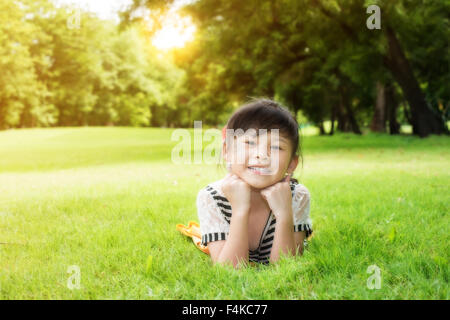 Poco ragazza asiatica che stabilisce sull'erba verde Foto Stock