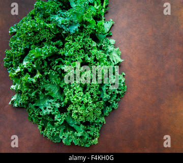 Mazzetto di crudo fresco verde pianta di cavolo riccio sulla tabella marrone Foto Stock