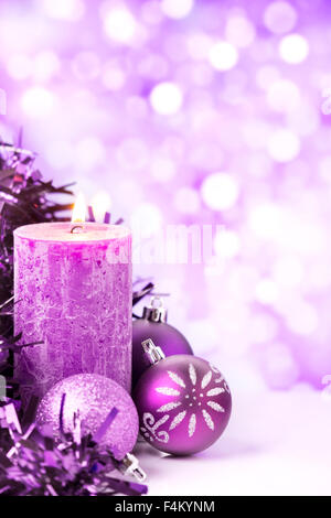 Viola e argento baubles di Natale e una candela di fronte defocalizzata viola e luci bianche. Foto Stock