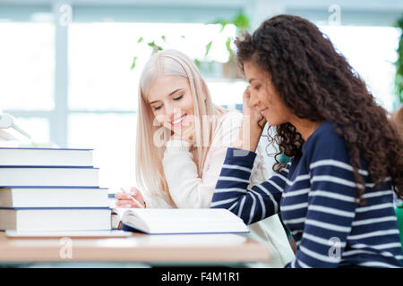 Sorridono due donne che svolgono compiti insieme nella biblioteca universitaria Foto Stock